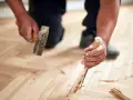 Un artisan utilise un ciseau et un marteau pour changer une lame de parquet flottant endommagée.