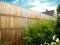 Clôture anti bruit en bois, haute et solide, protégeant un jardin verdoyant. Le ciel bleu et les nuages ajoutent une touche de sérénité.