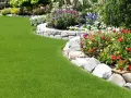 Magnifique pelouse verte bordée de fleurs colorées et d'une murette en pierres, parfaite pour faire bordure jardin.
