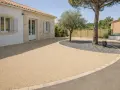 Allée de maison avec béton désactivé de belle épaisseur, bordée de pierres et de gravier sombre autour d'un arbre.