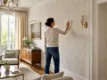 Une femme nettoie un mur avec un papier peint à motifs de feuilles. Elle utilise un chiffon pour peindre sur du papier peint, peut-être pour le rafraîchir.