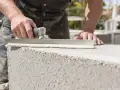 Un maçon applique du mortier sur un bloc de béton cellulaire extérieur pour la construction d'un mur.