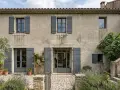 Maison en pierre avec volets gris, idéale pour une aide pour isolation extérieure. Jardin fleuri et pavé devant.