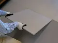 Pose d'une nouvelle dalle pour coller du carrelage sur du carrelage. Les mains gantées ajustent la pièce sur le sol existant.