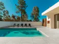 Une piscine moderne avec un sol en carrelage gris clair, des chaises longues et un barbecue extérieur sous un ciel bleu éclatant.
