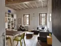Salon avec poutres apparentes au plafond, une personne lisant dans un fauteuil, canapé, table et étagères.