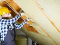 Un ouvrier en casque jaune réalise l'isolation des rampants par l'extérieur avec de la laine de roche.