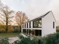 Agrandissement maison ossature bois moderne avec panneaux solaires, entourée d'arbres aux couleurs d'automne et d'un jardin enneigé.