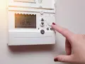 Main d'une femme ajustant un cee thermostat connecté affichant 18.4°C.