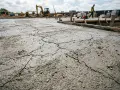 Une fissure dans une dalle de béton fraîchement coulée sur un chantier. Des engins de chantier sont visibles en arrière-plan.