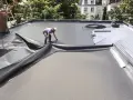 Un ouvrier pose une membrane pour l'étanchéité d'une terrasse en béton. Le travail est en cours.
