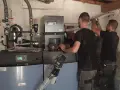 Techniciens installant une nouvelle chaudière, remplaçant une ancienne chaudière fioul. Travaux de chauffage en cours.