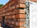 Mur en briques rouges, avec un plan de construction affiché. Le mortier sans retrait assure une pose parfaite.