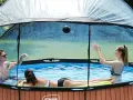 Trois personnes jouent dans une piscine hors sol sous un abri transparent. Idéal pour savoir comment fabriquer un abri piscine hors sol.