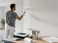 Un peintre applique une couche de peinture blanche sur un mur. Il utilise un rouleau et une boîte de peinture. On se demande combien de litre de peinture par m2 sera nécessaire pour ce chantier.