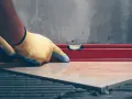 Pose d'un carrelage avec un niveau à bulle pour vérifier l'épaisseur du carrelage et de la colle.