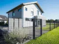 Une clôture privative en limite de propriété délimite un jardin moderne avec une maison blanche et un portillon.