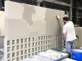 Un homme applique un enduit sur un mur en parpaings creux. L'épaisseur de l'enduit est visible par les zones plus claires et plus sombres.
