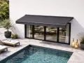 Un store banne gris protège une terrasse moderne avec piscine. L'entretien de ce store est essentiel pour profiter de cet espace de détente.