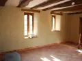 Intérieur d'une pièce aux poutres apparentes, murs en chaux chanvre pour une isolation naturelle, sol carrelé.
