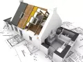 Maquette d'une maison en cours de rénovation, montrant la structure du toit et l'intérieur, posée sur des plans d'architecte. Un projet pour réhabiliter une maison.