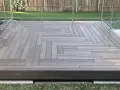 Une belle pose terrasse bois sur terre, avec un motif en chevrons moderne et des garde-corps en verre.