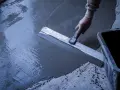 Main d'un ouvrier réalisant un ragréage de terrasse extérieur avec une lisseuse, assurant une pente pour l'évacuation de l'eau.