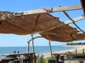 Installation d'une voile d'ombrage en toile de jute sur une structure en bois, offrant une vue sur la mer et la plage.