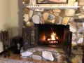 Un feu crépite dans une cheminée en pierres. Quel parement derrière poêle à bois, avec des accessoires de cheminée à gauche.