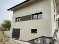 Maison moderne avec enduit neuf, une trace blanche discrète sur le crépi clair. Fenêtres noires et garage gris.