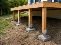 Vue d'un schema plan terrasse sur pilotis en bois, soutenue par des piliers en béton sur un terrain en pente.