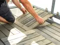 Un homme installe des dalles de terrasse en bois sur son balcon. Une belle idée sol balcon pour un espace extérieur accueillant.