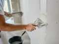 Un ouvrier applique de l'enduit sur une bande de placo. La question "faut-il humidifier les bandes placo" est au cœur de ce travail de finition.