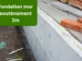 Construction d'un mur de soubassement de 2m, avec des briques rouges et des matériaux isolants.