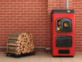 Une chaudière biomasse, c'est quoi ? Une chaudière rouge vif avec du bois de chauffage à côté, prête à chauffer.