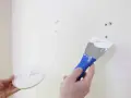 Main tenant en main une spatule chargée de mastic, prêt à reboucher trou mur.