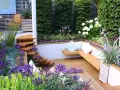 Magnifique terrasse en bois avec banquette intégrée, escalier en colimaçon et fleurs violettes. Idéal pour fabriquer banquette bois terrasse.