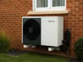 Une pompe à chaleur monobloc Atlantic, fixée au mur de briques d'une maison, avec des tuyaux noirs et un ventilateur visible.