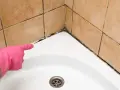 Main rose avec un gant, montrant la moisissure sur le joint de la baignoire. Il est temps d'enlever moisissure joint.