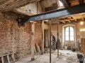 Un ouvrier travaille sous une poutre métallique soutenue par des étais, remplaçant un ipn mur porteur dans une maison en rénovation.