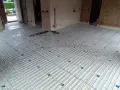 Installation d'un plancher chauffant en cours de renovation. Les tuyaux blancs sont posés sur des panneaux isolants, prêts à être recouverts.