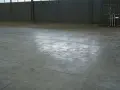 Vaste entrepôt avec une dalle béton qui part en poussière, marquée par des traces de passage.