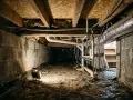 Éclairage d'un vide sanitaire humide, révélant des tuyaux, des conduits et des murs en blocs de béton.