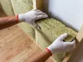 Mains gantées installent un isolant pour aider à isoler un mur humide.