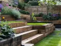 Jardin aménagé en terrasses sur un terrain en pente raide, avec des parterres de fleurs colorées et de l'herbe verte vive.