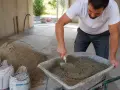 Un ouvrier mélange du ciment dans une brouette, préparant un chape maigre dosage pour une construction.