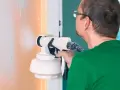 Un homme en t-shirt vert utilise un pistolet pour peindre un mur en orange.