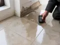 Un professionnel mesure l'humidité au sol carrelage près d'un mur endommagé par l'eau.