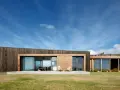 Maison moderne en bois avec grande baie vitrée, deux chaises invitantes sur la terrasse. Une extension maison container stylée.
