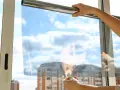 Application d'un film pour l'isolation des fenêtres. Mains tenant un film transparent devant une fenêtre avec un ciel bleu et des nuages.